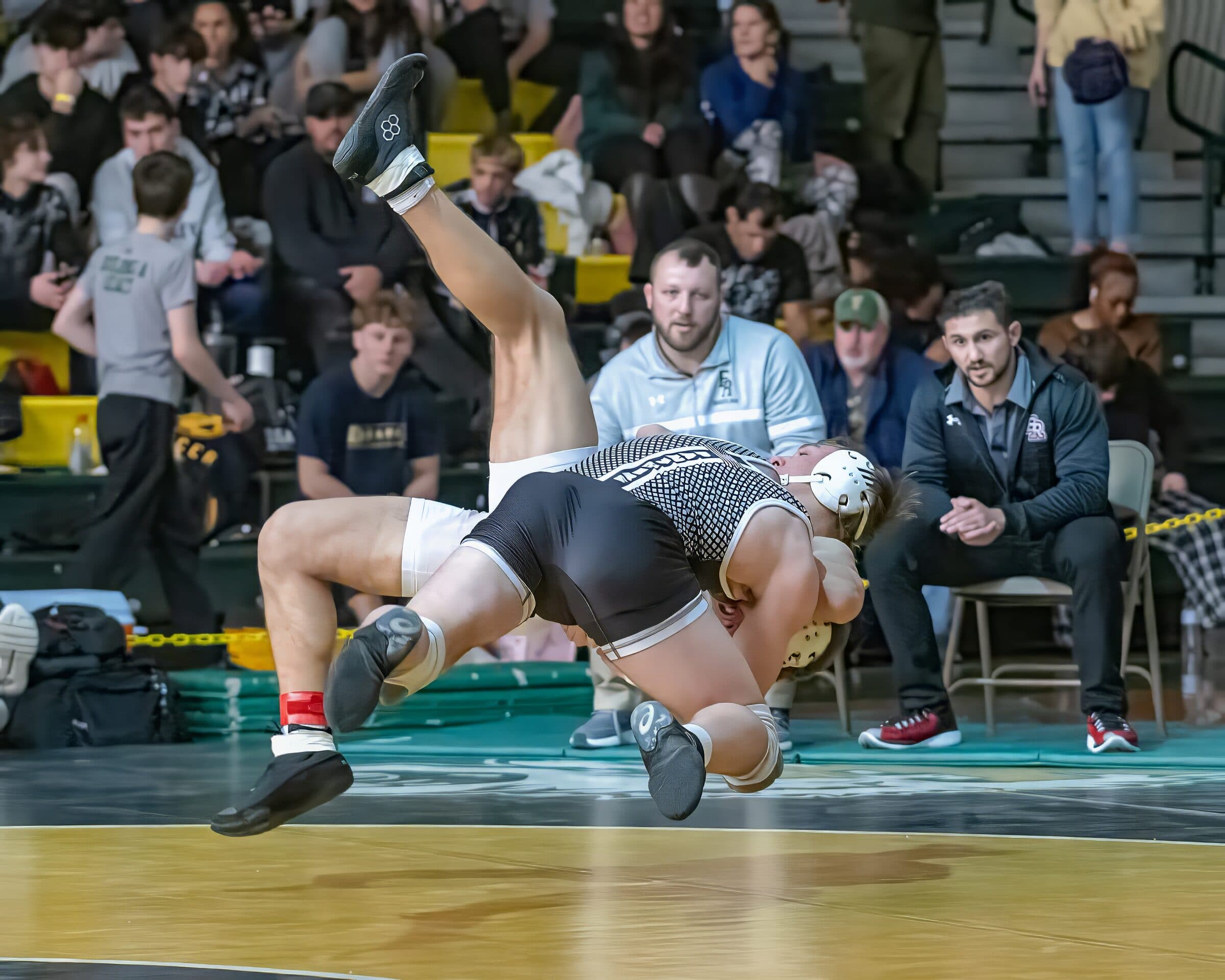 Wrestler drives opponent to the mat in a packed gym